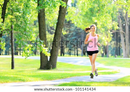 Jogging woman running in park in sunshine on beautiful summer day. Sport fitness model of mixed Asian / Caucasian ethnicity training outdoor for marathon.