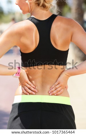 Back pain. Sports injury fitness woman in black sportswear rubbing muscles of her lower back, touching sport accident doing massage, torso from behind. Girl sweating wearing smartwatch.