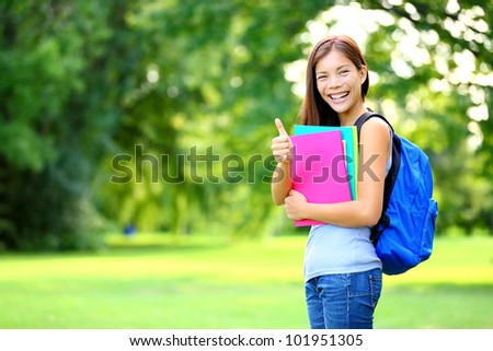 Student in park showing happy thumbs up success sign. Mixed race Asian Caucasian woman university student holding books outside.