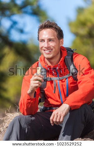 Hiker man healthy outdoor lifestyle eating muesli bar during hike on mountain hiking. Happy people eat granola cereal bar snack living active lifestyle in nature.