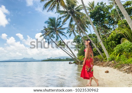 Tahiti luxury travel beach vacation woman walking in polynesian cover-up skirt beachwear on idyllic paradise island in French Polynesia. Red traditional clothes, bikini and flower girl.