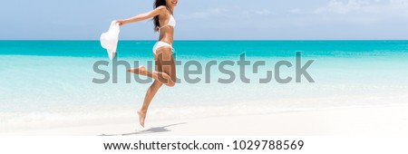 Happy beach body woman jumping of joy with sun hat on caribbean travel vacation. Slim legs sexy bikini girl sun tanning feeling free. Banner panorama with copy space on blue ocean background