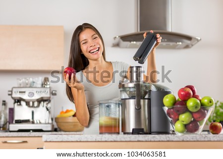 Vegetable juice healthy food juicer machine- Asian woman juicing green and red apple fruits as part of her wellness food, detox smoothie. Beautiful happy mixed Asian woman with juice maker in kitchen.
