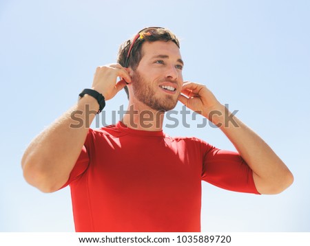 Young man putting on wireless headphone bluetooth connected to smartwatch earphones for fitness run outdoors. Happy active person wearing earbuds for exercise.