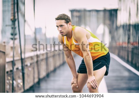 Tired runner taking a break breathing during jogging workout training on Brooklyn bridge in New York City, NYC active healthy lifestyle. Man running outdoors.