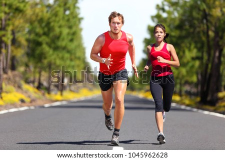 Running fitness couple of runners doing sport on road outdoor. Active living man and woman jogging training cardio in summer outdoors nature. Asian girl, caucasian athletes.