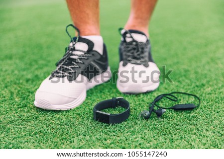 New technology sport wearable accessories for runners: fitness sports smart watch and wireless earphones man running shoes. Earbuds, smartwatch on grass. Tech run gear, smart jogging.