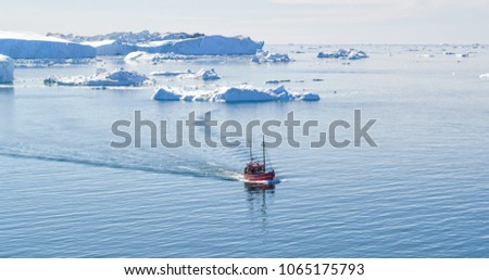 Icebergs and tourist fishing boat in Greenland iceberg landscape of Ilulissat icefjord with giant icebergs. Icebergs from melting glacier. Aerial drone photo of arctic nature.