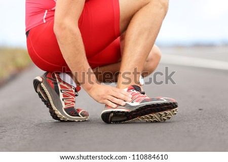 Broken twisted ankle - running sport injury. Male runner touching foot in pain due to sprained ankle. - stock photo