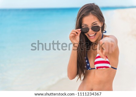 Sexy American Asian woman wearing USA flag bikini swimsuit clothing for 4th of july independence day beach party vacation on summer vacation. Happy girl having fun pointing choosing you .