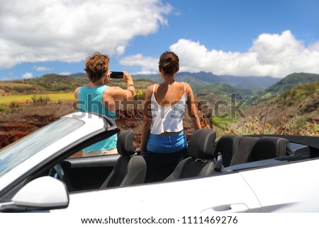 Road trip car people taking phone pictures of nature landscape on summer travel vacation. Tourists couple taking photos on Hawaii Kauai island, with smartphone camera app.