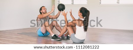 Gym fitness couple training body core together throwing weight ball at each other during sit-ups on floor workout panoramic banner.