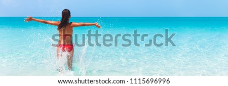 Summer fun beach woman splashing water with open arms banner. Panorama landscape of tropical ocean on travel holiday. Bikini girl running in freedom and joy with hands up enjoying the sun.