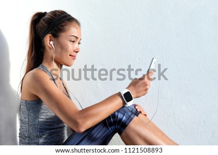 Fitness Asian girl using earphones phone watching video on cellphone wearing smartwatch. Technology in fitness active lifestyle.
