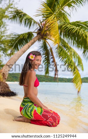 Beach woman relaxing on Bora Bora Tahiti island under the sun wearing polynesian skirt and monoi flower with palm tree background. Polynesia culture travel concept.