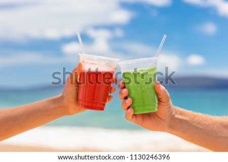 Healthy juice smoothie drinking couple toasting cold pressed organic drinks together at beach restaurant. Detox smoothie drink toast at summer vacations holidays. Fruit juicing weight loss diet.