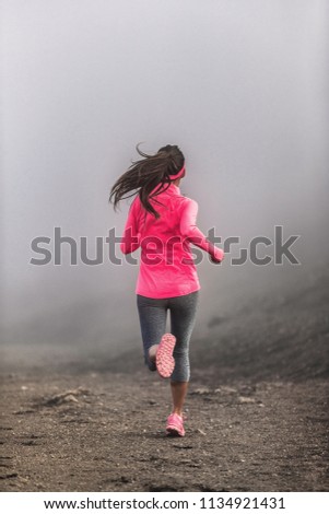 Run fit woman runner running on trail path in mountains in fog and clouds - morning jogging training in pink sportswear clothes.