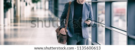 Business man texting on mobile phone commuting walking in airport with messenger bag using cellphone texting sms message on smartphone app - young businessman commute lifestyle panoramic banner.