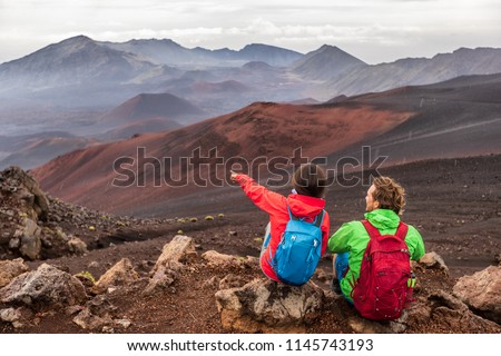 Hiking travel vacation in Maui volcano, Hawaii. USA travel woman with backpack pointing at Haleakala volcano landscape. Couple tourists resting outdoors.