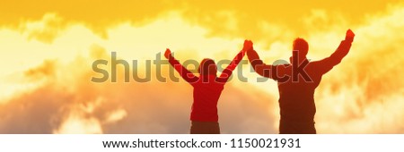 Happy winners reaching life goal - success people at summit. Business achievement concept. Two person couple together arms up in air in the clouds at sunset panoramic banner.
