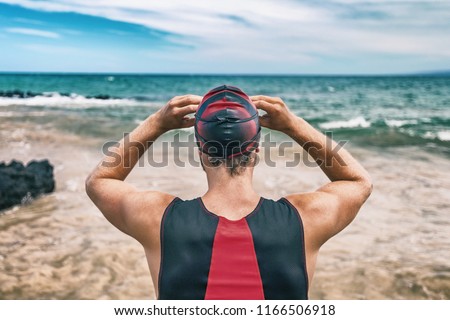 Triathlon swim sport man on race . Swimmer getting ready for open ocean competition. Triathlete from behind putting goggles.