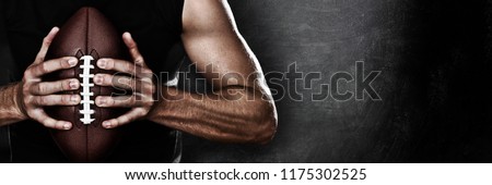 Football player man player holding american football on black blackboard texture background with copy space for text or design. Panoramic banner.