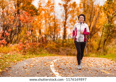 Middle age active and healthy Asian woman exercising weight loss body workout jogging running in park path autumn forest. Middle aged lifestyle. Lady in her 50s.