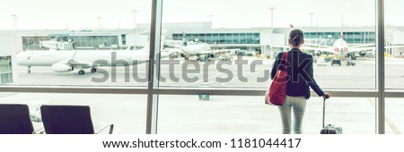 Traveler businesswoman at airport banner. Travel lifestyle. Travel tourist standing with luggage at airport lounge. Unrecognizable woman looking at window waiting at boarding gate before departure.