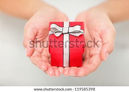 Gift. Woman holding showing gift or christmas gift in her hands. Female hands giving red present.