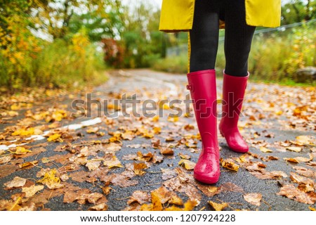 Autumn fall city lifestyle colorful leaves and red rain boots woman feet walking in park outside.