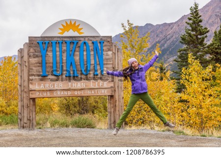 Yukon territory welcome sign - happy tourist woman jumping of fun in canadian territories. Alaska cruise travel autumn holiday.