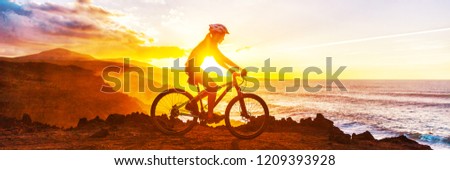Mountain biking cyclist riding bike on coast trail against sunset. Silhouetter of woman doing sports outdoors banner panorama. Active lifestyle.