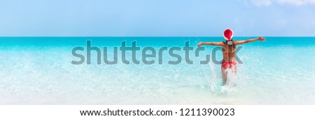 Christmas Caribbean beach tropical Santa Claus woman Happy swimming in blue ocean water panorama banner. Bikini girl with pen arms freedom carefree. Travel vacation holidays under the tropical sun.