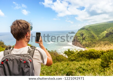 Travel tourist man in Hawaii beach USA vacation taking photo with mobile phone device of ocean landscape mountains background. Big Island, Hawaii.