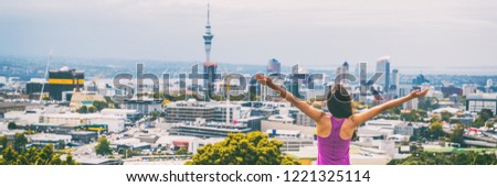 Auckland city happy woman in New Zealand banner. Skyline view from Mount Eden of Sky tower, arms up in freedom and happiness at top of Mt Eden urban park famous tourist attraction.