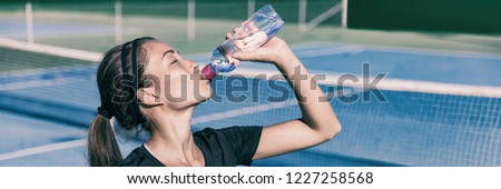 Thirsty Sporty Asian girl drinking water while playing tennis on outdoor court. Sports active lifestyle woman hydrating with water sports bottle. Panorama banner.