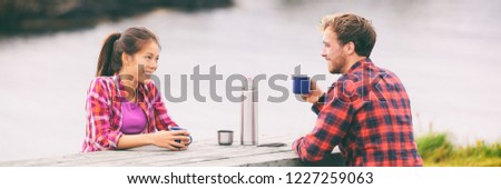 Camping happy couple drinking coffee on morning breakfast table at campsite enjoying summer tourism holidays. Asian tourist woman with man, outdoor.