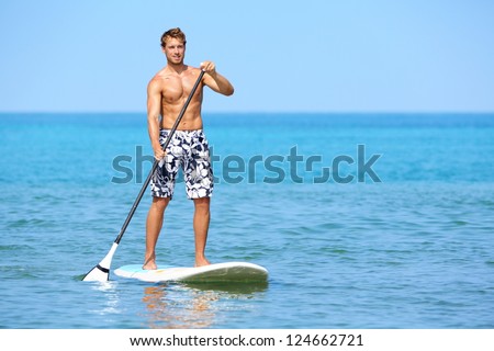 Stand Up Paddle Board Man Paddleboarding On Hawaii Standing Happy On Paddleboard On Blue Water. Young Caucasian Male Model On Hawaiian Beach On Summer Holidays Vacation Travel.