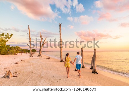 Couple walking on beach at sunset romantic travel getaway, idyllic Florida destination, Lovers key beach state park in the gulf of Mexico. Woman and man holding hands relaxing. Southwest Florida.