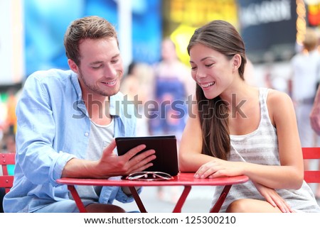 Multiethnic couple dating in New York City on Times Square. Man showing woman tablet pc smiling happy together.