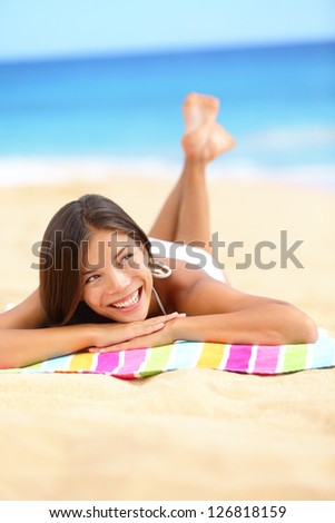 Vacation beach woman lying down relaxing and looking to the side and up. Happy smiling girl in bikini lying on sand on beach towel during summer travel holidays.