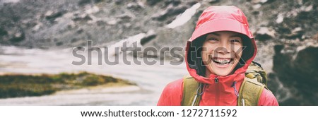 Active outdoors people lifestyle - happy hiker Asian woman laughing in the rain on mountain hike - Outdoors adventure trek activity, wearing waterproof raincoat sportswear clothes. Banner panorama.