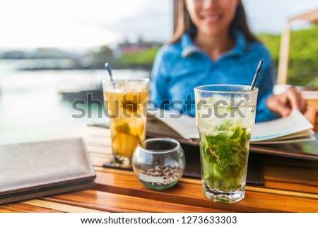 Two alcoholic cocktails at beach restaurant outside on dining table. Woman and closeup of drink mojito cocktail.