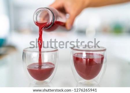 Juice bottle beet drink smoothie woman pouring drinks in cups at home kitchen. Closeup of two glasses with red vegetable juicing cold pressed beverage.