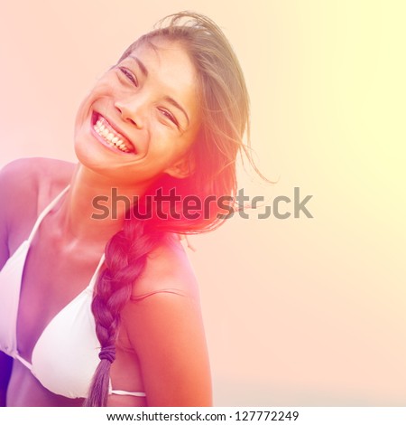 Happy Sunshine Woman. Girl Smiling Joyful, Friendly And Charming Looking At Camera On Warm Sunny Summer Day Under The Hot Sun On Beach. Beautiful Multicultural Asian / Caucasian Female Bikini Model.