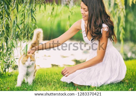 Cat woman cute spring portrait petting her animal outsisde in garden grass green park. Asian girl pet owner caressing kitten. Summer lifestyle outdoor.