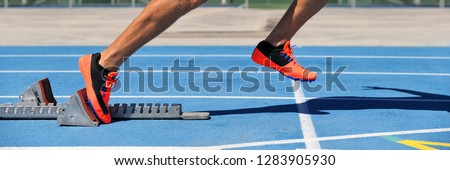 Track spikes shoes feet on starting blocks on running track and field stadium blue lanes. Sprinting man athlete runner at run start leaving at the beginning of the race competition. Banner crop.