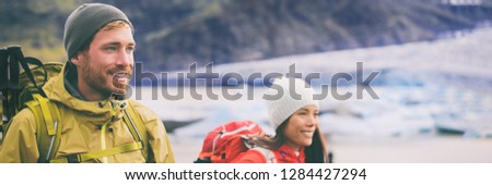 Two hikers people walking together hiking in wilderness. Alpine climbers mountaineering couple trekking in ice snow mountains. Panorama banner of team hiking in winter.