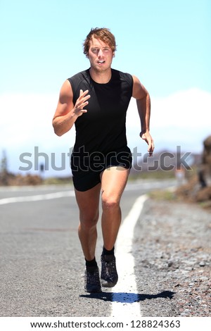 Fit handsome muscular young man jogging on a country road running directly towards the camera with a look of determination