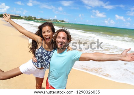 Happy people jumping screaming of fun on beach summer vacation travel in Hawaii. Laughing young Asian woman with Caucasian man, tourists couple friends on holiday.